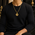 A man wearing a black long-sleeve shirt and a gold chain necklace with a round pendant featuring an Om symbol, set against a dark, elegant background.
